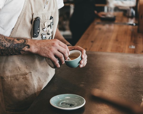 Barista podává šálek cappuccina přes dřevěný pult.
