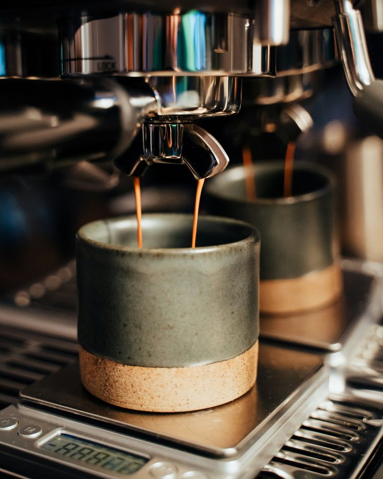 Espresso steče dvojitým výtokem do kameniných šálků na váze.