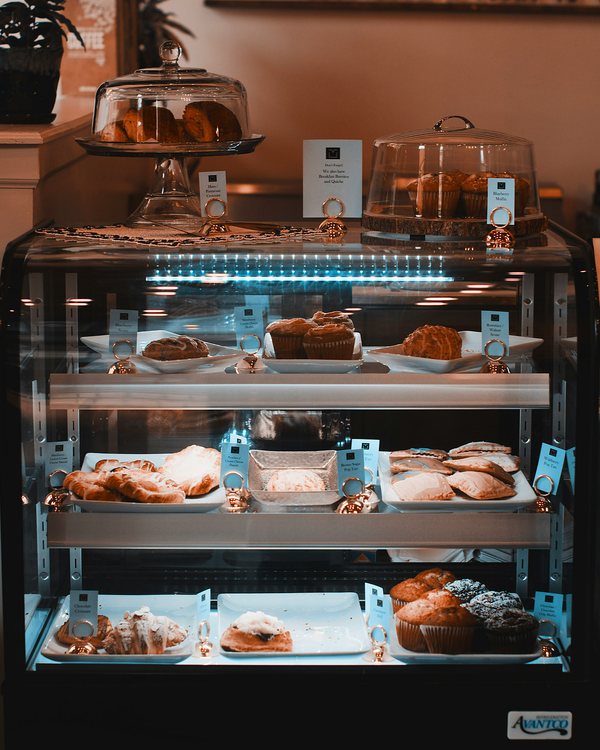 Prosklená vitrína s koláči, croissanty a muffiny.